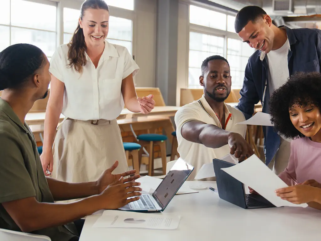 Team som samarbetar runt datorer och dokument i en modern arbetsmiljö