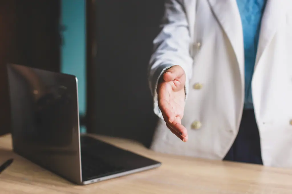 En bärbar dator på ett bord med en hand som sträcks fram ovanför ytan.