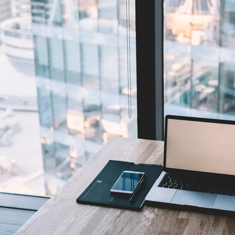 Arbetsplats med laptop, surfplatta och smartphone placerade på skrivbord i kontorsmiljö med utsikt över stad