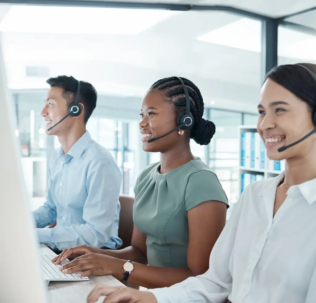 Tre personer med headset sitter vid arbetsplatser i ett ljust kontor med stora fönster.