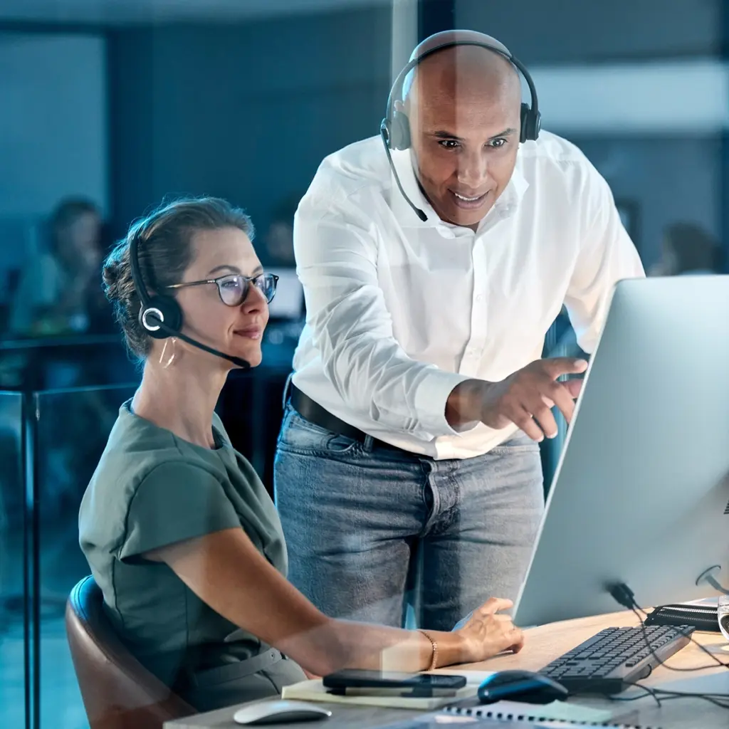Två personer med headset arbetar vid stor datorskärm, en person pekar på skärmen.