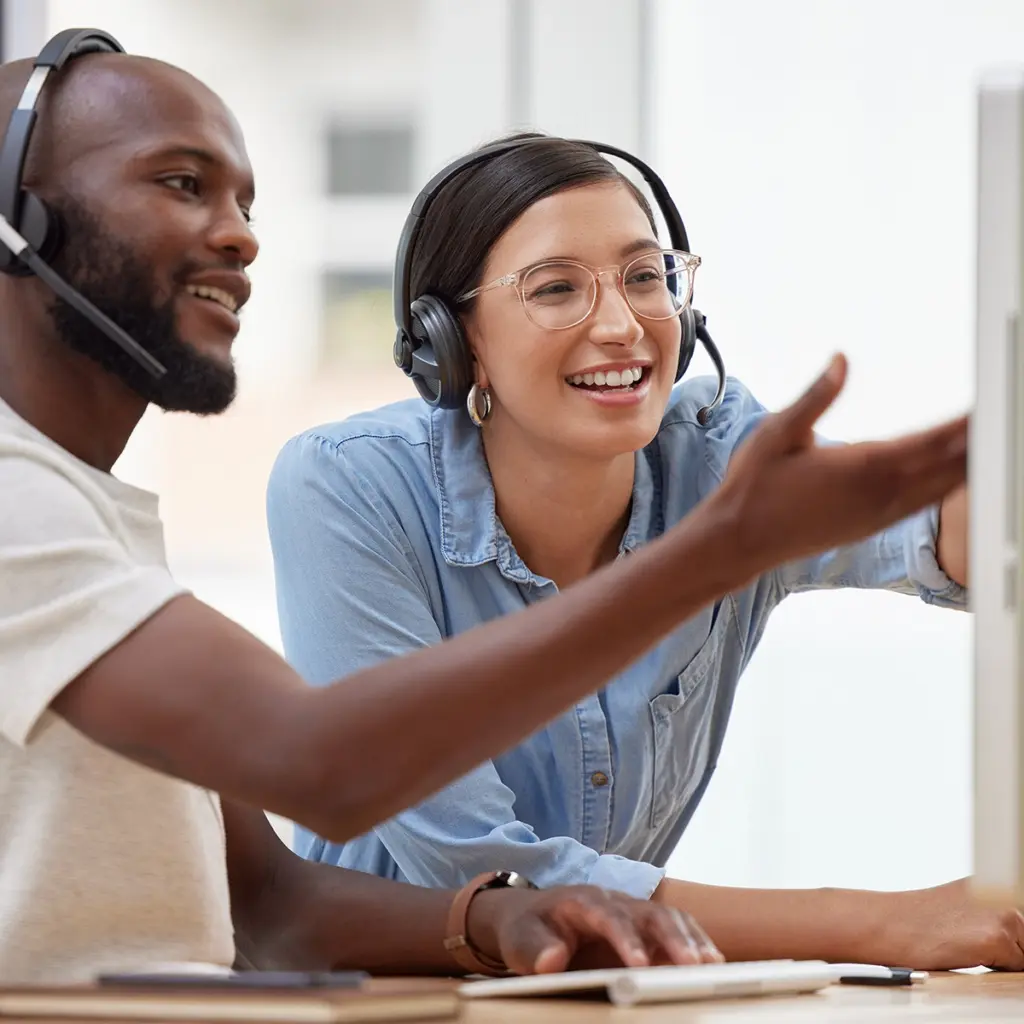 Två personer med headset arbetar vid dator och pekar mot skärm.
