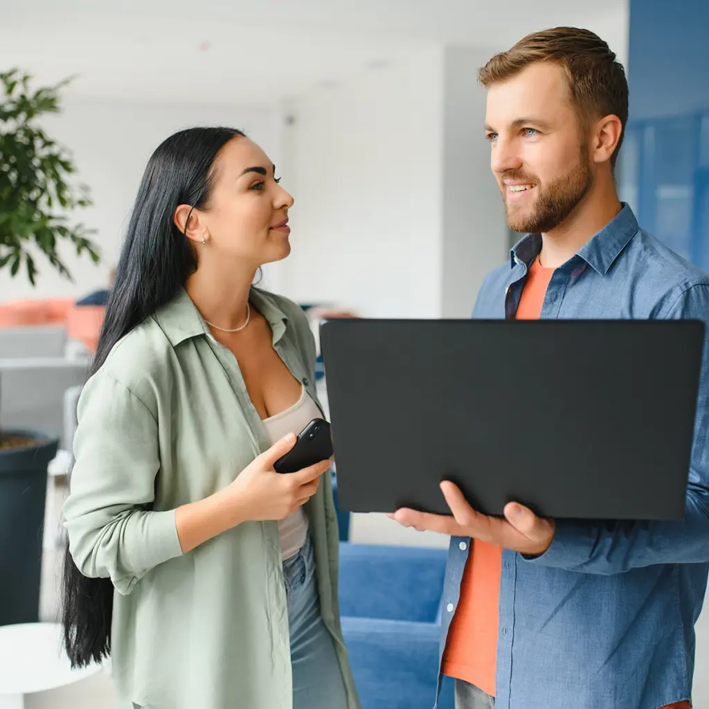 Två personer står tillsammans och tittar på en öppen laptop, en person håller en mobiltelefon.