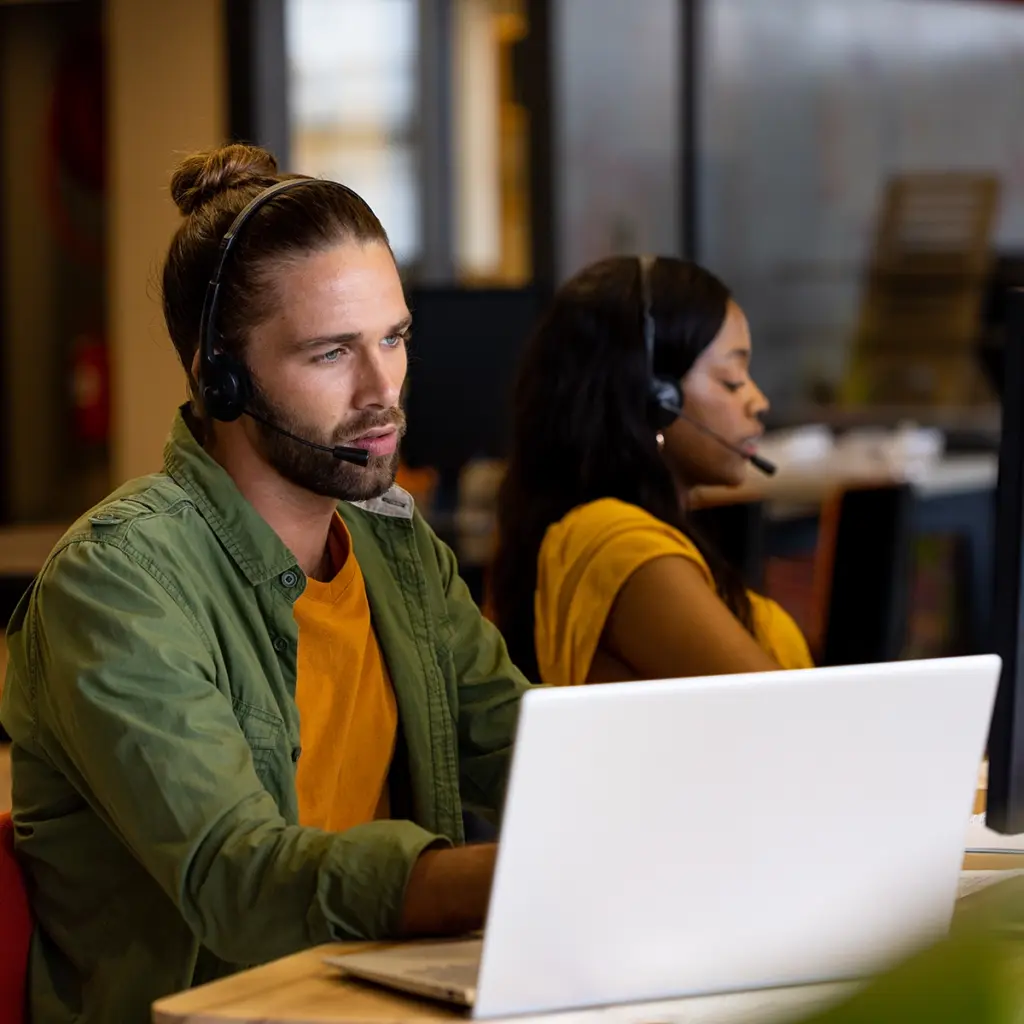 Två personer med headset sitter vid datorer i kontorsmiljö.