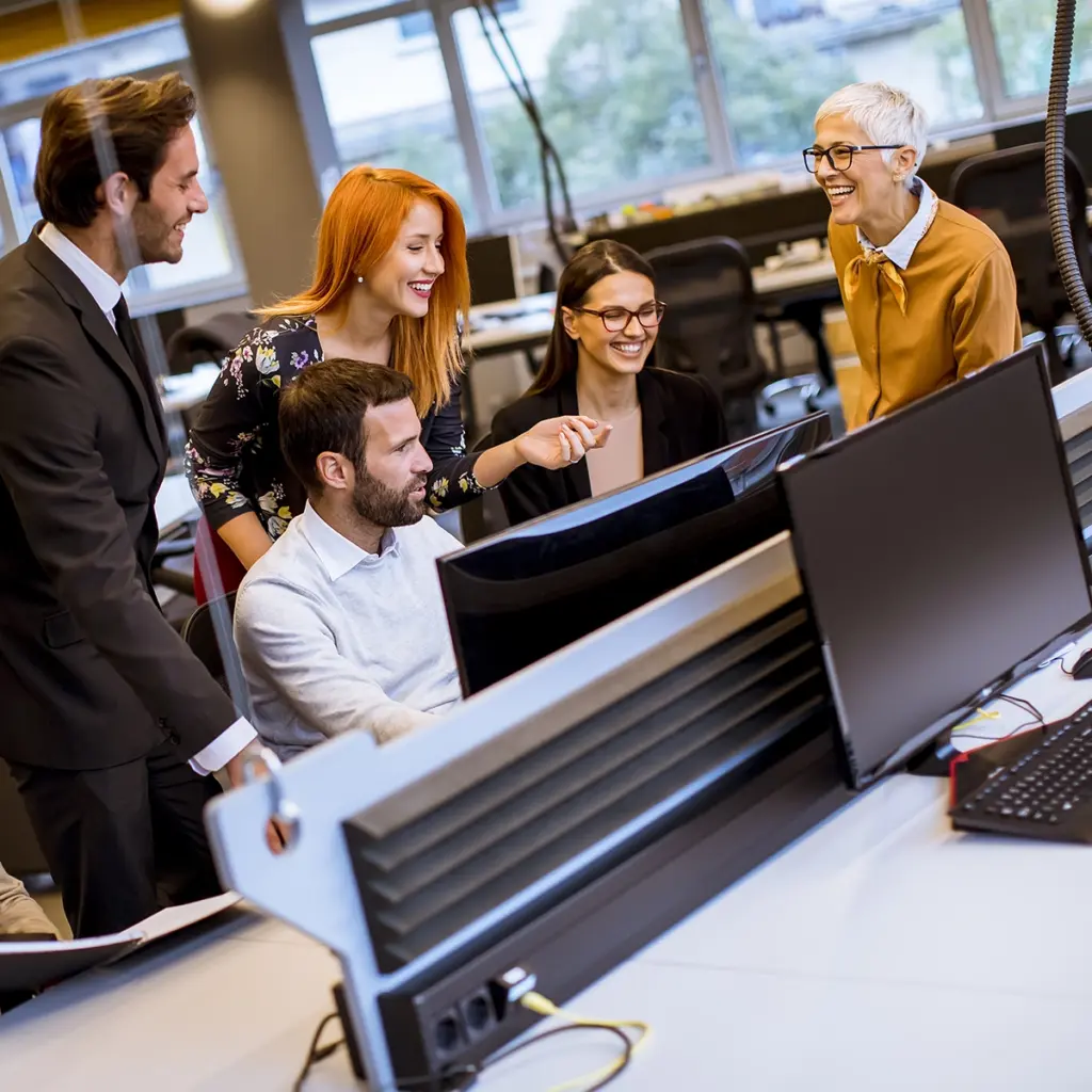 Flera personer står och sitter runt datorskärmar i ett öppet kontorslandskap.