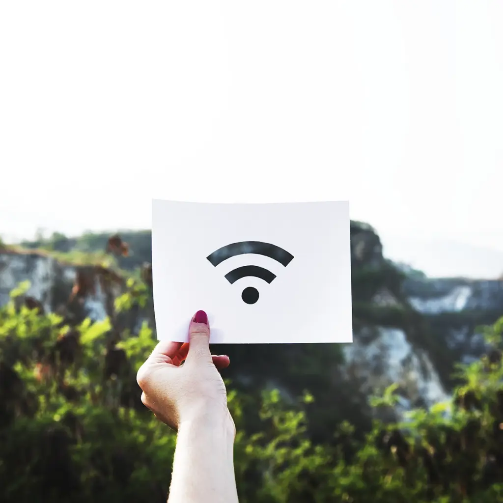Hand håller upp ett papper med wifi-symbol framför en suddig naturbakgrund.