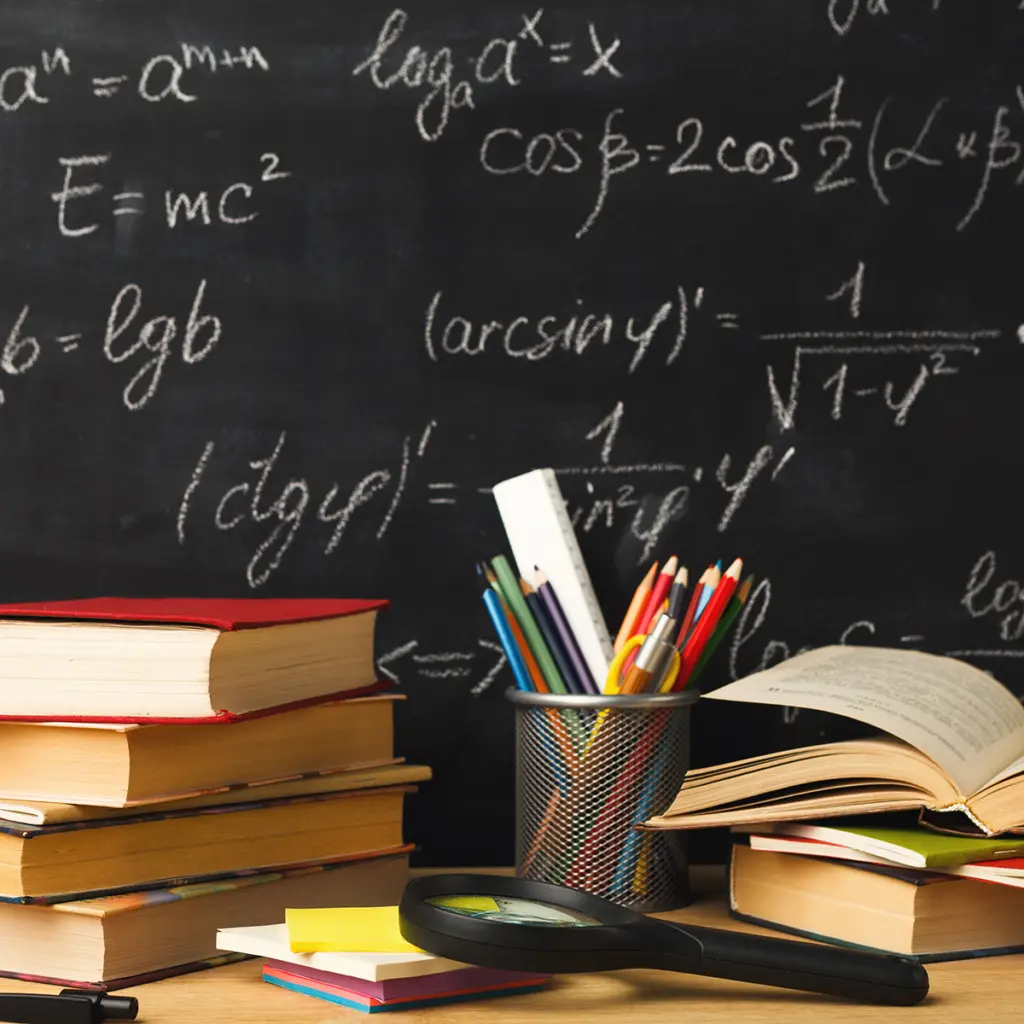 Böcker, pennor och förstoringsglas framför en griffeltavla med matematiska formler